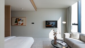 Et moderne hotelværelse med seng, sofa, sofabord, fjernsyn og et maleri på væggen.