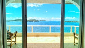 A room with a view of the sea, a balcony, and two wooden chairs.