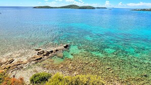 A coastal landscape with clear turquoise waters, rocky shorelines, and distant green islands.