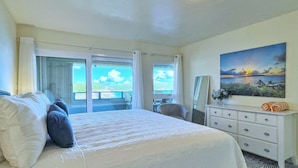 A hotel room with a bed, a dresser, a mirror, and a painting of a sunset over water.