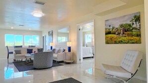 A spacious living room with a large window, a sofa set, a coffee table, and a patterned rug.