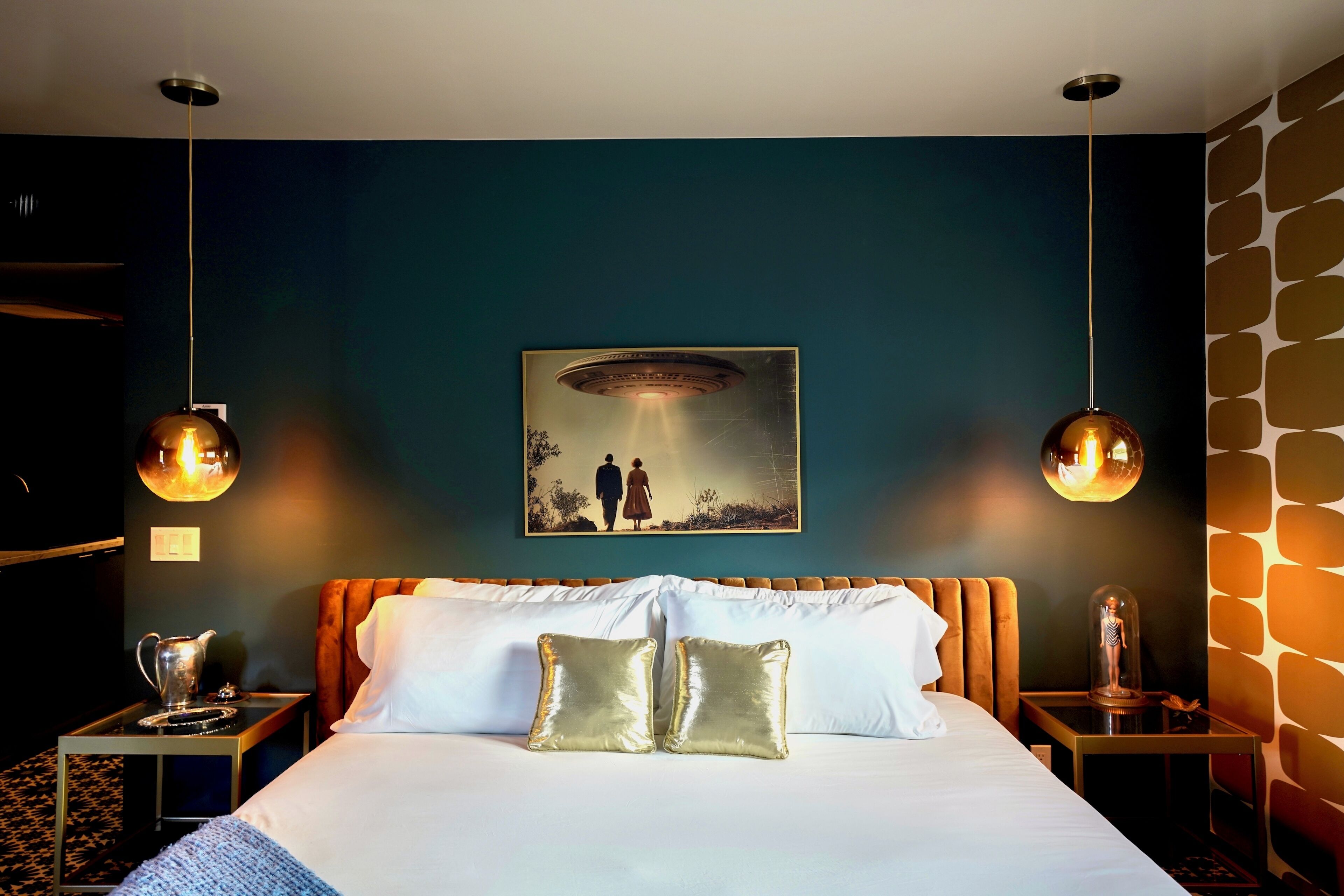 Une chambre d’hôtel avec un lit, deux lampes de chevet, un tableau et un papier peint à motifs.