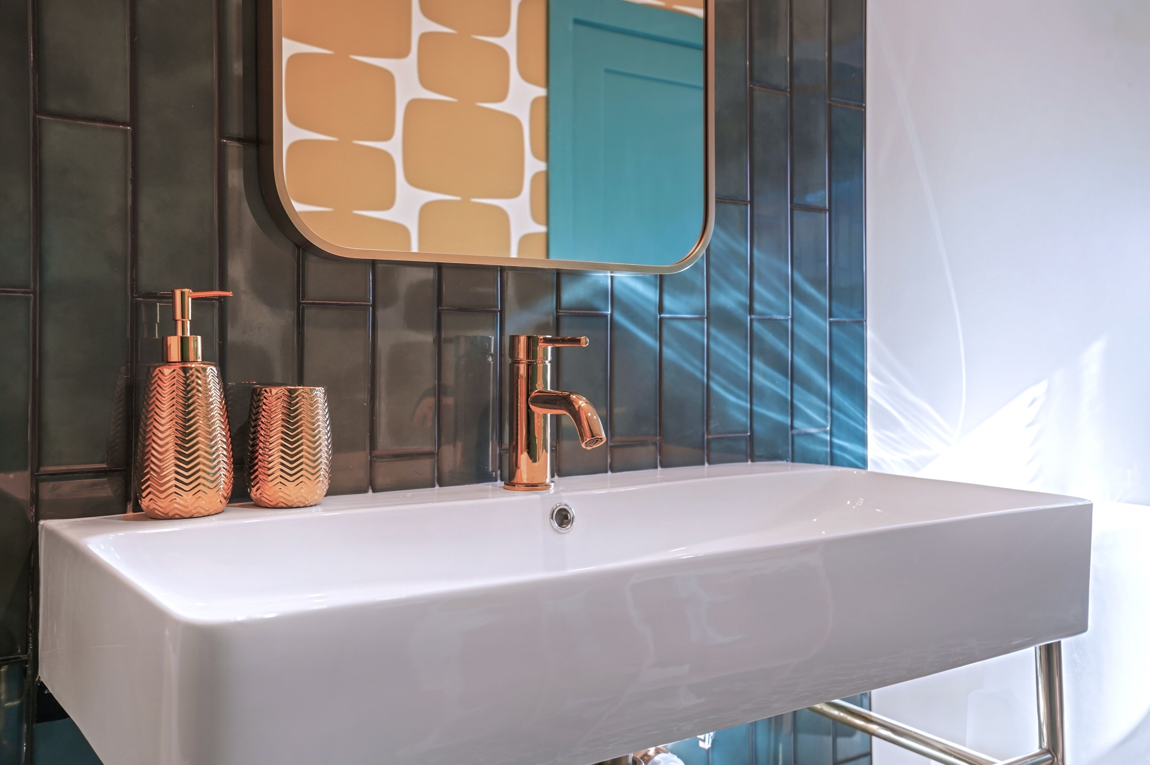 A bathroom with a white sink, copper faucet, and two patterned bottles.