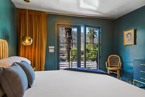Ein Schlafzimmer mit einem Bett, einem Sessel, einem Schminktisch und Blick durch eine Tür.