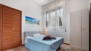 Un dormitorio con cama, ventana con cortinas translúcidas, un cuadro de playa y un armario.