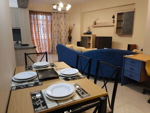 Un espace repas avec une table dressée pour quatre personnes, un canapé, un téléviseur et un coin cuisine avec un comptoir.