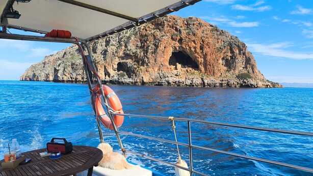 A boat with a table and life preserver, a rocky island in the background, and a clear blue sea. - Odysseas Nea Chora Apartment with Sea View, Wi-Fi and Air Conditioning (Chania)