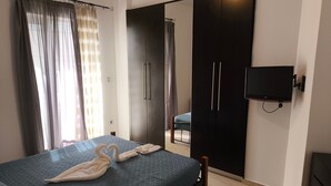 A bedroom with a bed, a wardrobe, a television, and a bathroom visible through an open door. - Odysseas Nea Chora Apartment with Sea View, Wi-Fi and Air Conditioning (Chania)