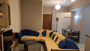 A living room with a sectional sofa, a coffee table, a TV, and a dining area with chairs and a table. - Odysseas Nea Chora Apartment with Sea View, Wi-Fi and Air Conditioning (Chania)