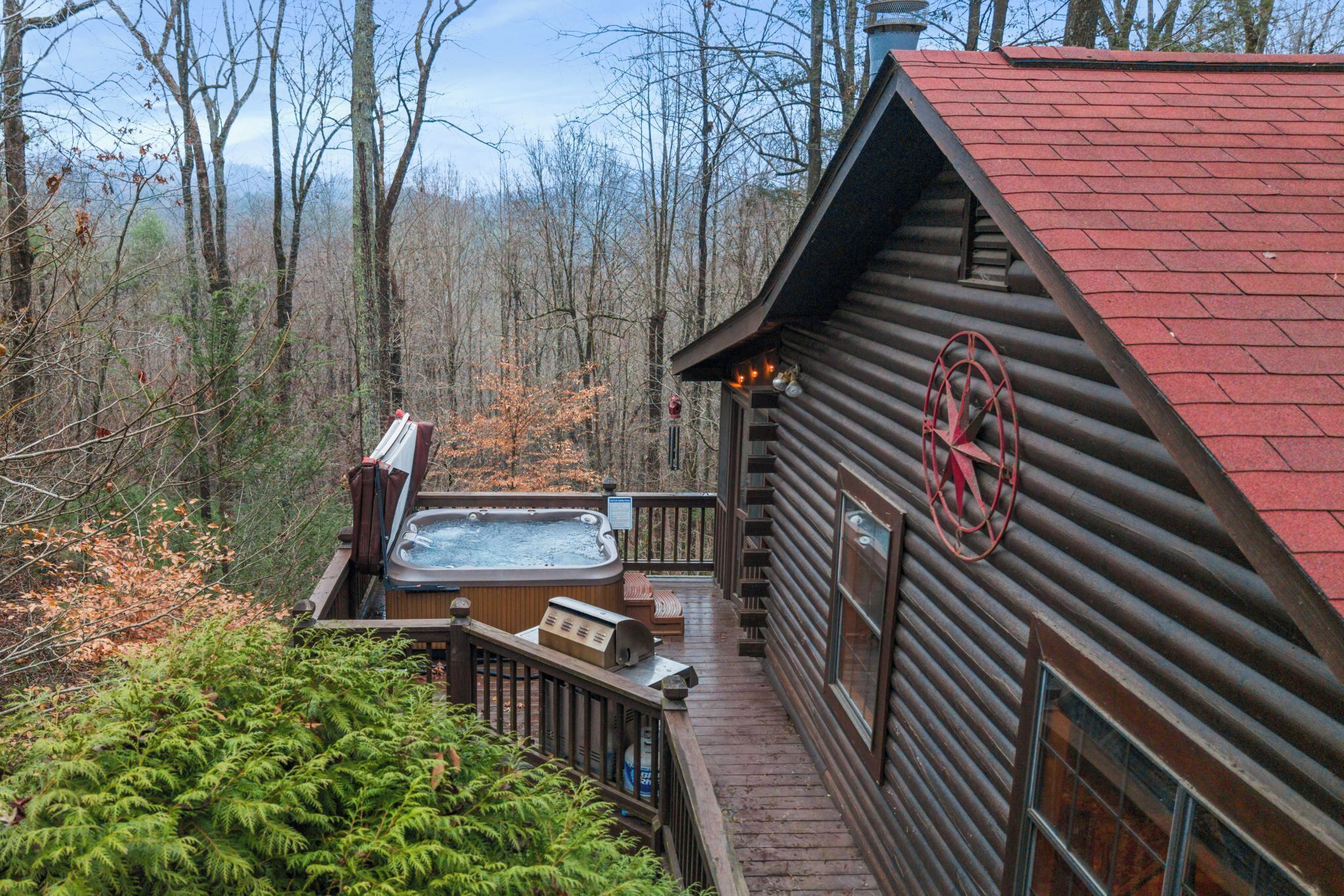 A log cabin with a hot tub on a deck, surrounded by trees.