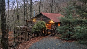 A rustic cabin with a wooden deck and a chimney, surrounded by trees and a gravel path. - Mountain Views, Hot Tub + More! - Deer Crossing (Ellijay)