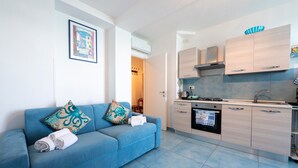 Una cocina moderna con horno empotrado y microondas, un sofá azul con cojines decorativos y un cuadro en la pared.
