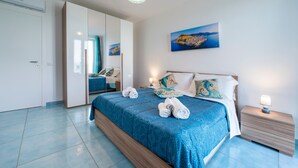 Un dormitorio con cama, mesita de noche, espejo, un cuadro y una puerta.