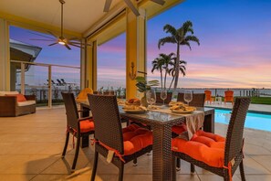 Enjoy meals with a view of the ocean from this dining area, featuring a wicker table and chairs with comfortable cushions.