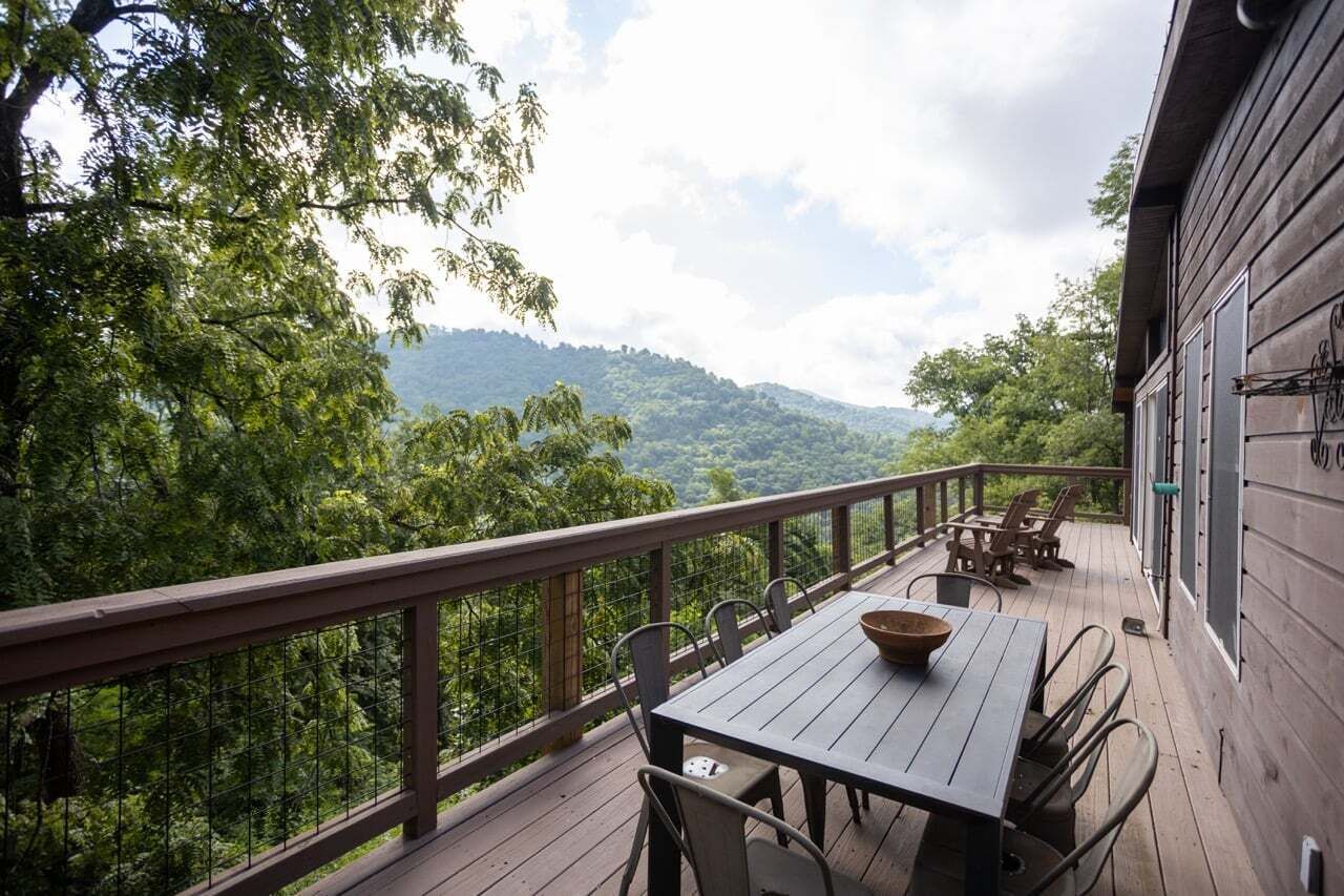 A wooden deck with a table and chairs, overlooking a forested landscape.