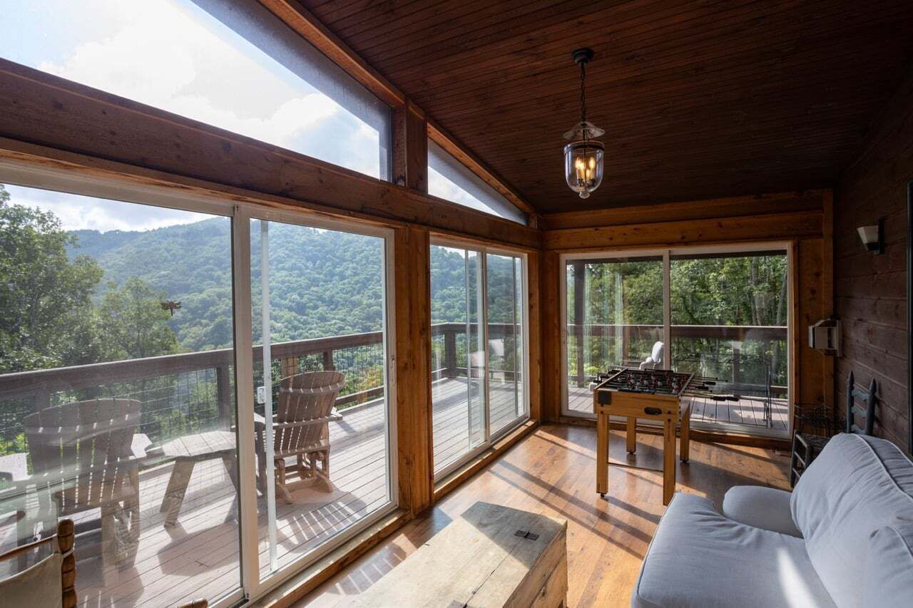 A wooden interior with large windows, a sofa, and a foosball table.