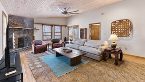 Ein Wohnzimmer mit Kamin, Deckenventilator, Sofa, Sesseln, Couchtisch und Fernseher.