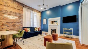 Een moderne woonkamer met een bakstenen muur, een blauwe accentmuur, een open haard, een televisie en een eethoek met een tafel en stoelen.