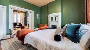 Een slaapkamer met een groot bed, een open haard en uitzicht op een andere kamer met een bank en een tafel.