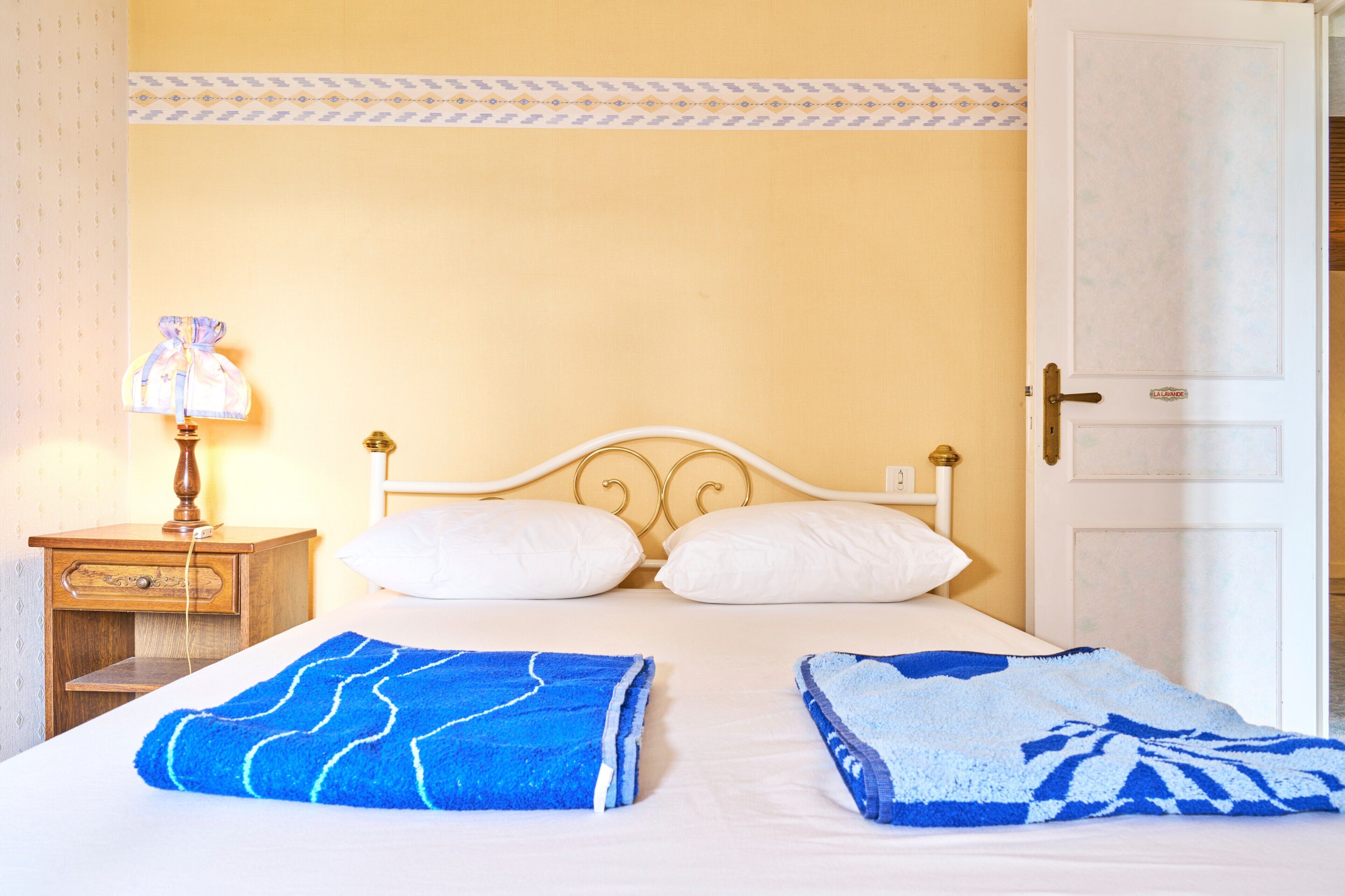 A bed with two towels, a nightstand with a lamp, and a door to the right.
