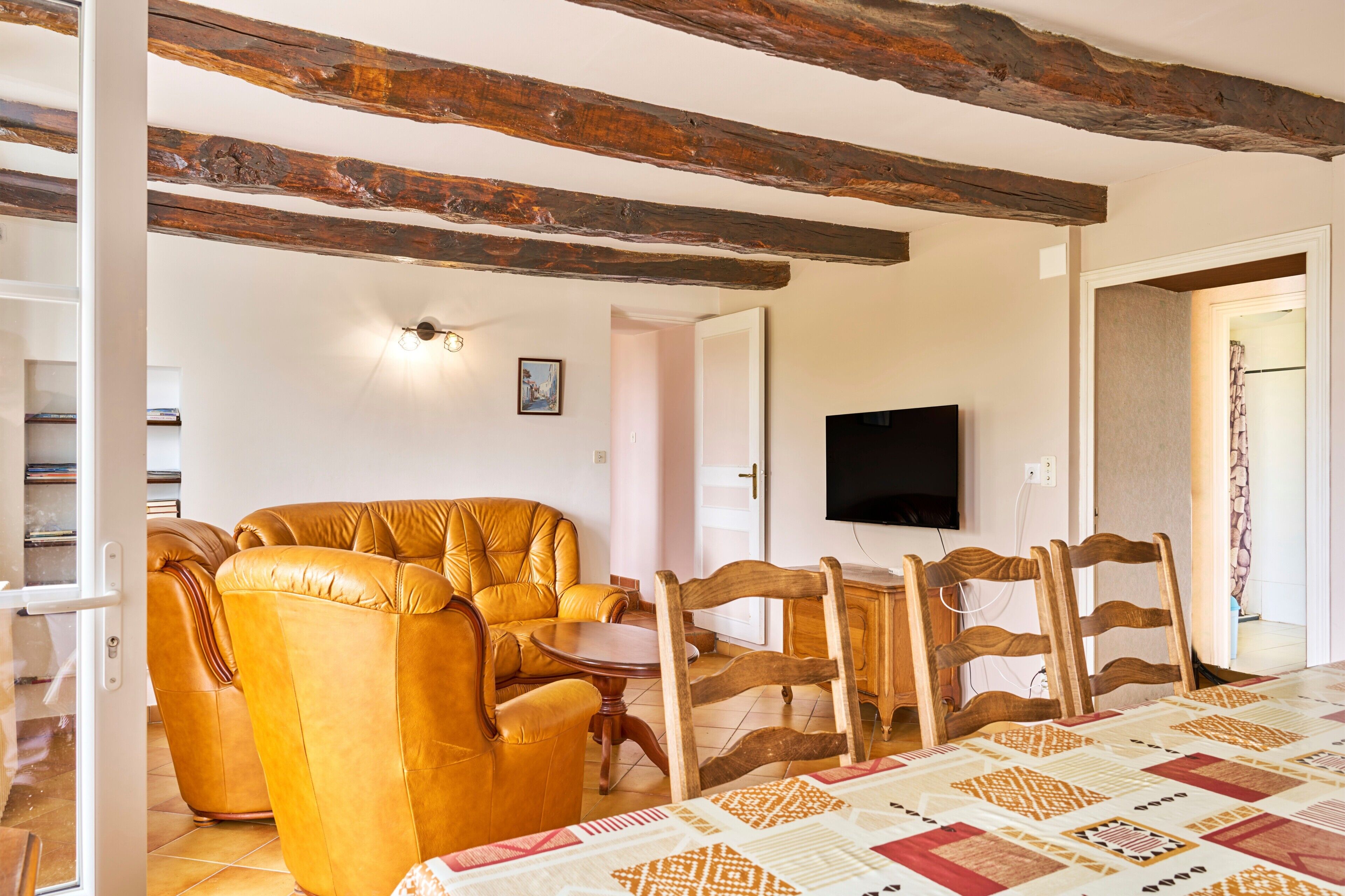 Una sala de estar con un sofá, sillas de madera, un televisor y un mantel acolchado.