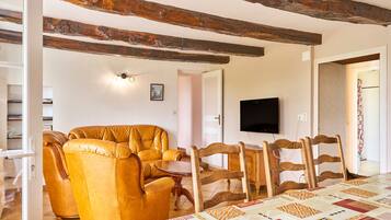Una sala de estar con un sofá, sillas de madera, un televisor y un mantel acolchado.