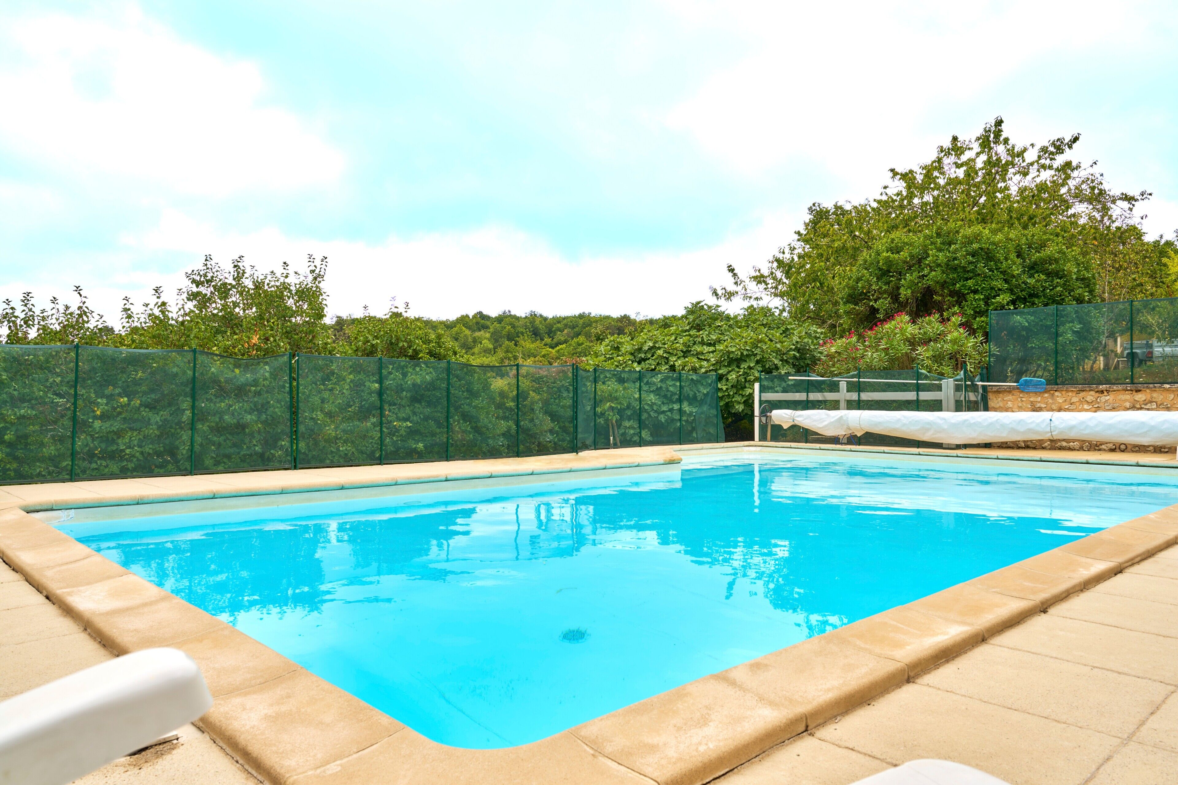 A rectangular swimming pool with a clear blue water surface, surrounded by a beige tiled deck.