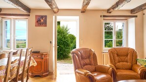 A room with a wooden dining table, two chairs, a leather armchair, and a view of greenery through a door.