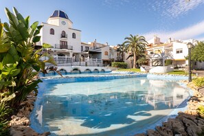 Une piscine avec une fontaine, entourée de bâtiments blancs dotés de balcons et d’un clocher.