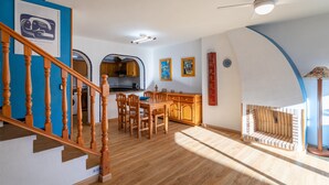 Una cocina moderna con armarios de madera, un comedor con mesa y sillas, una escalera con barandilla de madera y un ventilador de techo.
