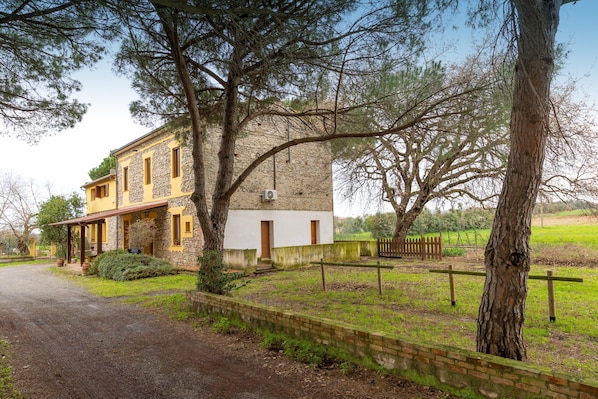 Un edificio de piedra de dos pisos con fachada amarilla, un camino de entrada pavimentado y un jardín cercado.