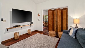 En moderne stue med et fladskærms-tv, trægulv, en grå sofa og et stort spejl.