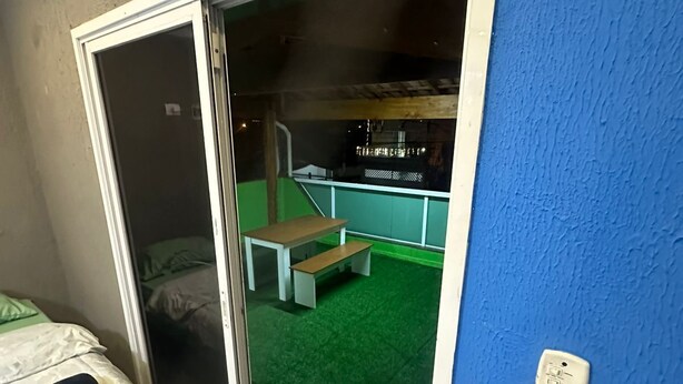 A room with a bed, a sliding glass door leading to an outdoor area with a bench and a green surface. - Moriah Pousada e  Hostel (Praia Grande)