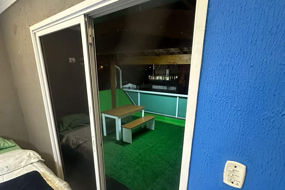 Una habitación con una cama, un ventanal corredero que da a un espacio exterior con una banca y superficie verde.