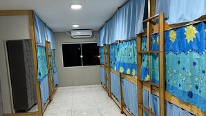 A hotel corridor with rows of rooms, each with a curtain and a number on the wall. - Moriah Pousada e  Hostel (Praia Grande)