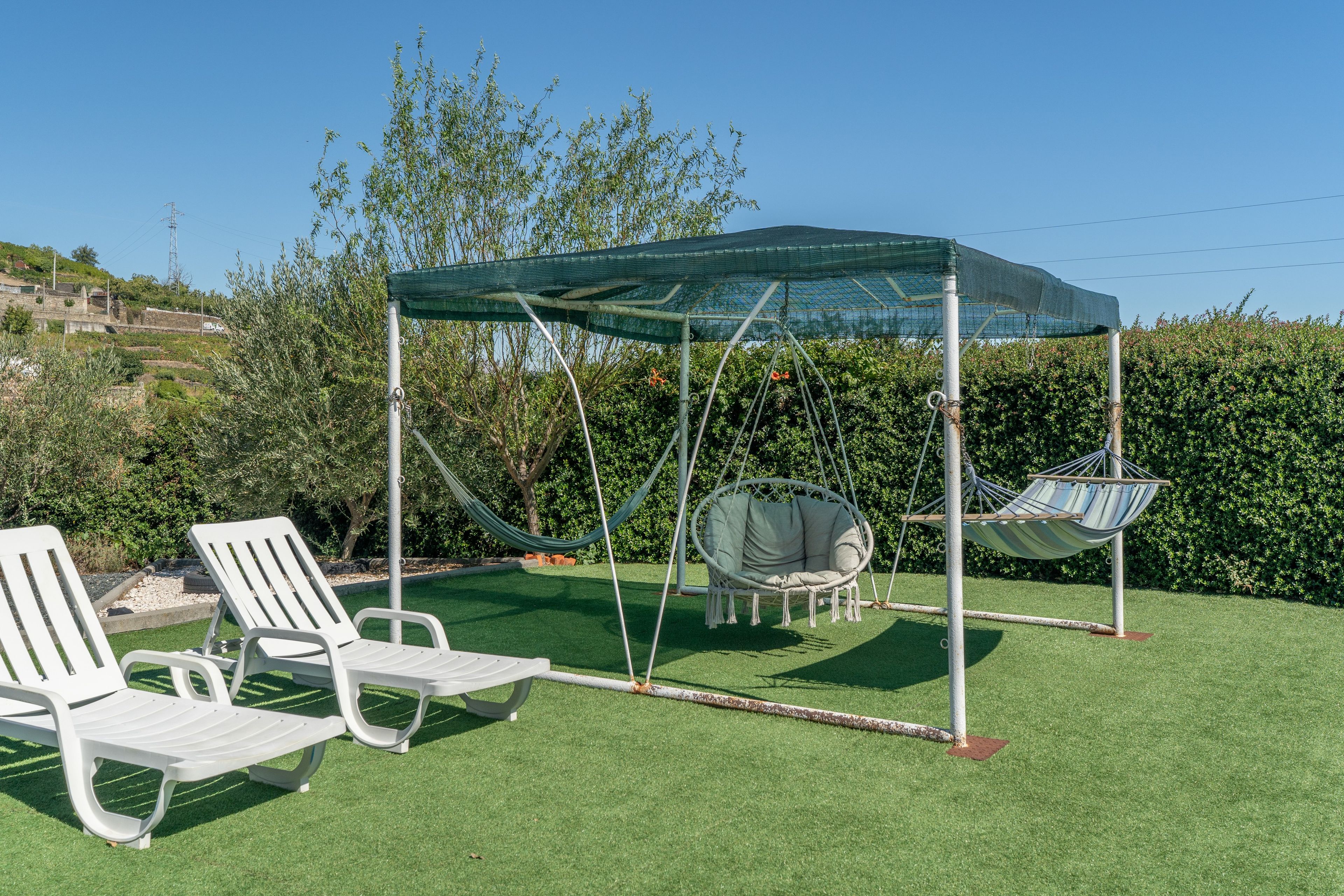Ein Garten mit Kunstgrashalm, einem Schaukelsessel und zwei Liegestühlen.