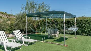 Ein Garten mit Kunstgrashalm, einem Schaukelsessel und zwei Liegestühlen.