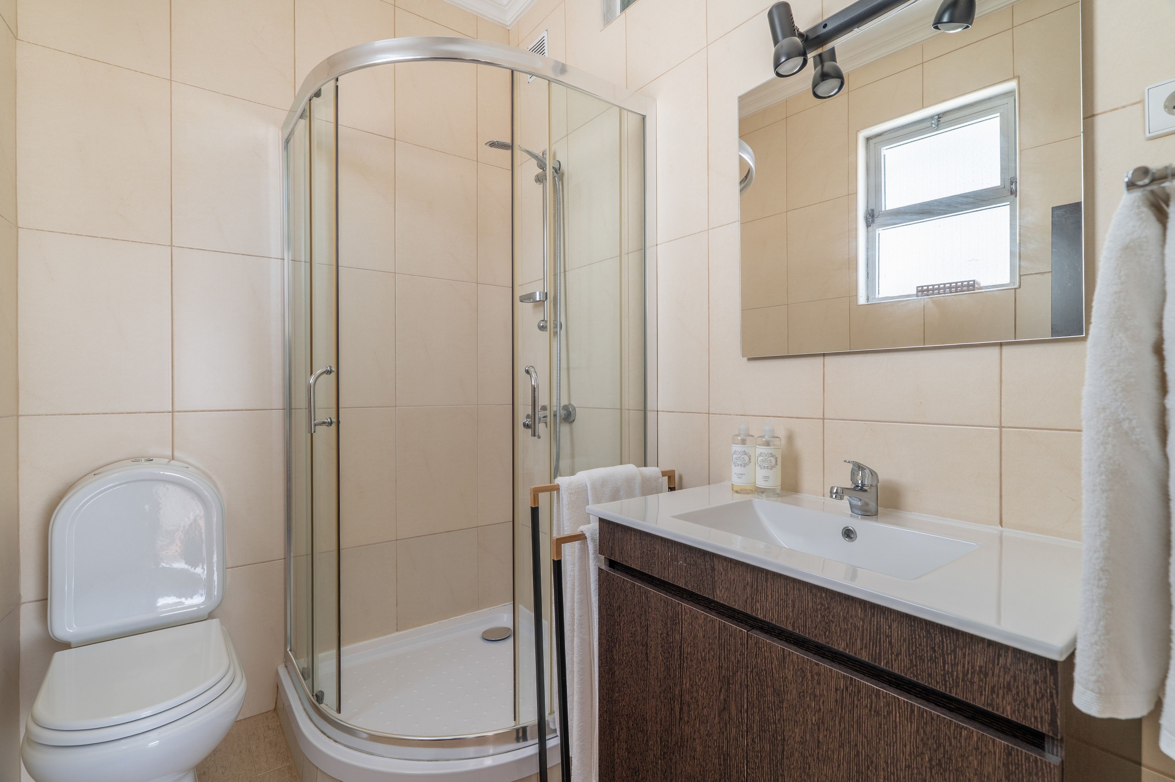 A bathroom with a glass-enclosed shower, a white toilet, a sink with a mirror above it, and a towel hanging on the wall.
