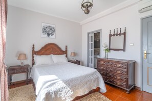 A bedroom with a wooden bed, two bedside tables, a dresser, a mirror, and a door. - Casa da Jesus with Mountain View, Wi-Fi, and Air Conditioning (Provesende)