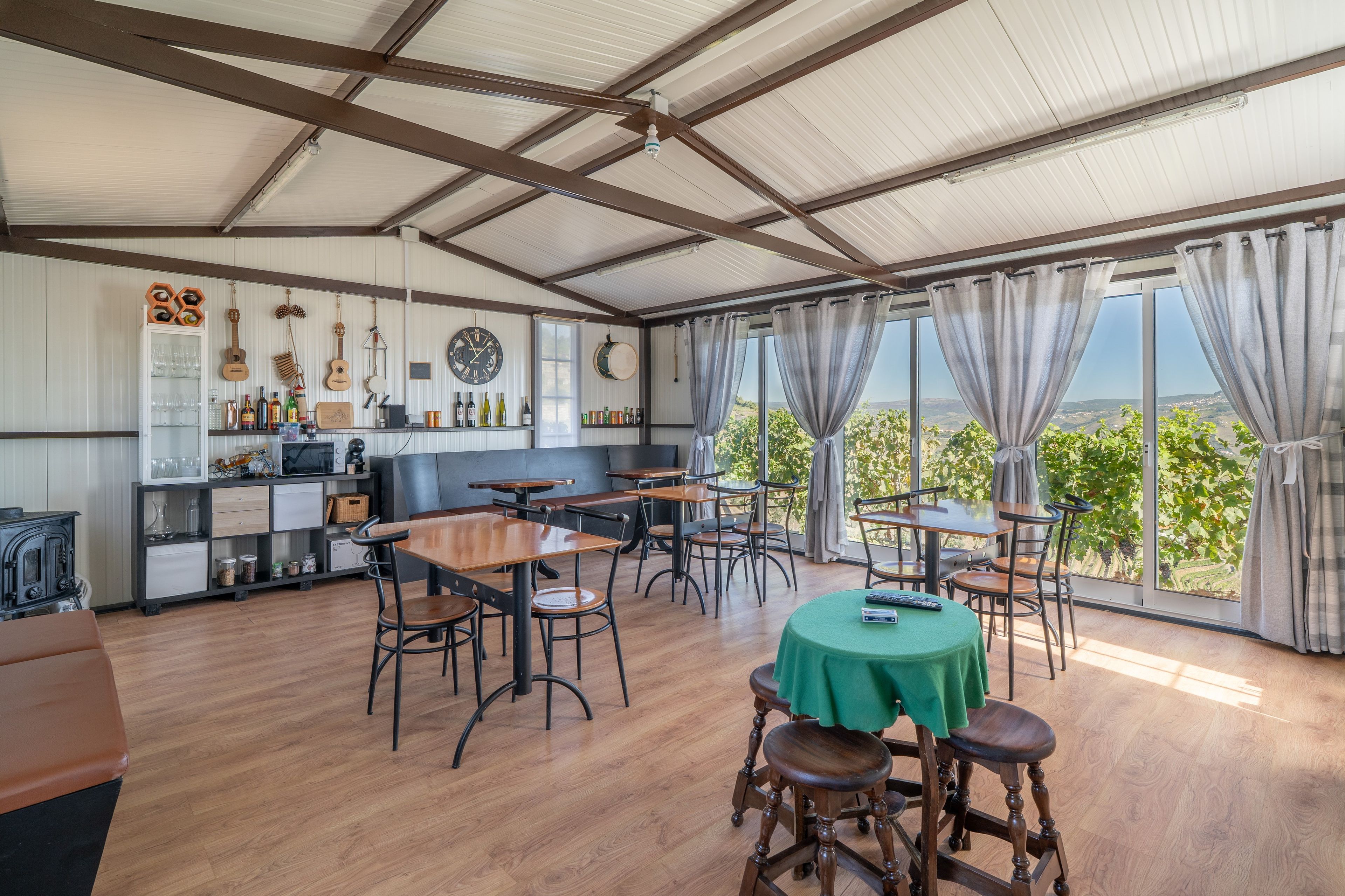 Ein geräumiger Raum mit hohen Decken, Holztischen und -stühlen, einem Tisch mit grüner Tischdecke und Blick auf die Landschaft durch große Fenster.