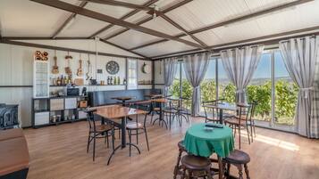 Ein geräumiger Raum mit hohen Decken, Holztischen und -stühlen, einem Tisch mit grüner Tischdecke und Blick auf die Landschaft durch große Fenster.