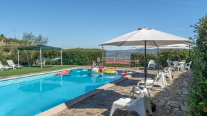 Una piscina con sillones de descanso y sombrillas, rodeada de baldosas de piedra y follaje.