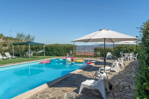 A swimming pool with lounge chairs and umbrellas, surrounded by stone tiles and greenery.