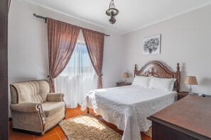 A bedroom with a bed, a chair, a nightstand, a lamp, and a painting on the wall. - Casa da Jesus with Mountain View, Wi-Fi, and Air Conditioning (Provesende)