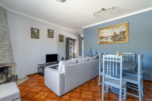 A living room with a grey sofa, a flat-screen TV, a fireplace, and a dining area with a white table and chairs. - Casa da Jesus with Mountain View, Wi-Fi, and Air Conditioning (Provesende)