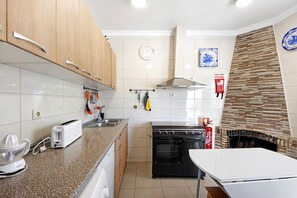 A kitchen with wooden cabinets, a white countertop, a toaster, an oven, a clock, and a fire extinguisher.