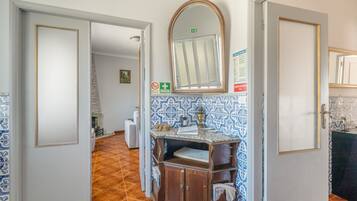 A hallway with a wooden cabinet, a mirror, and a tiled wall.