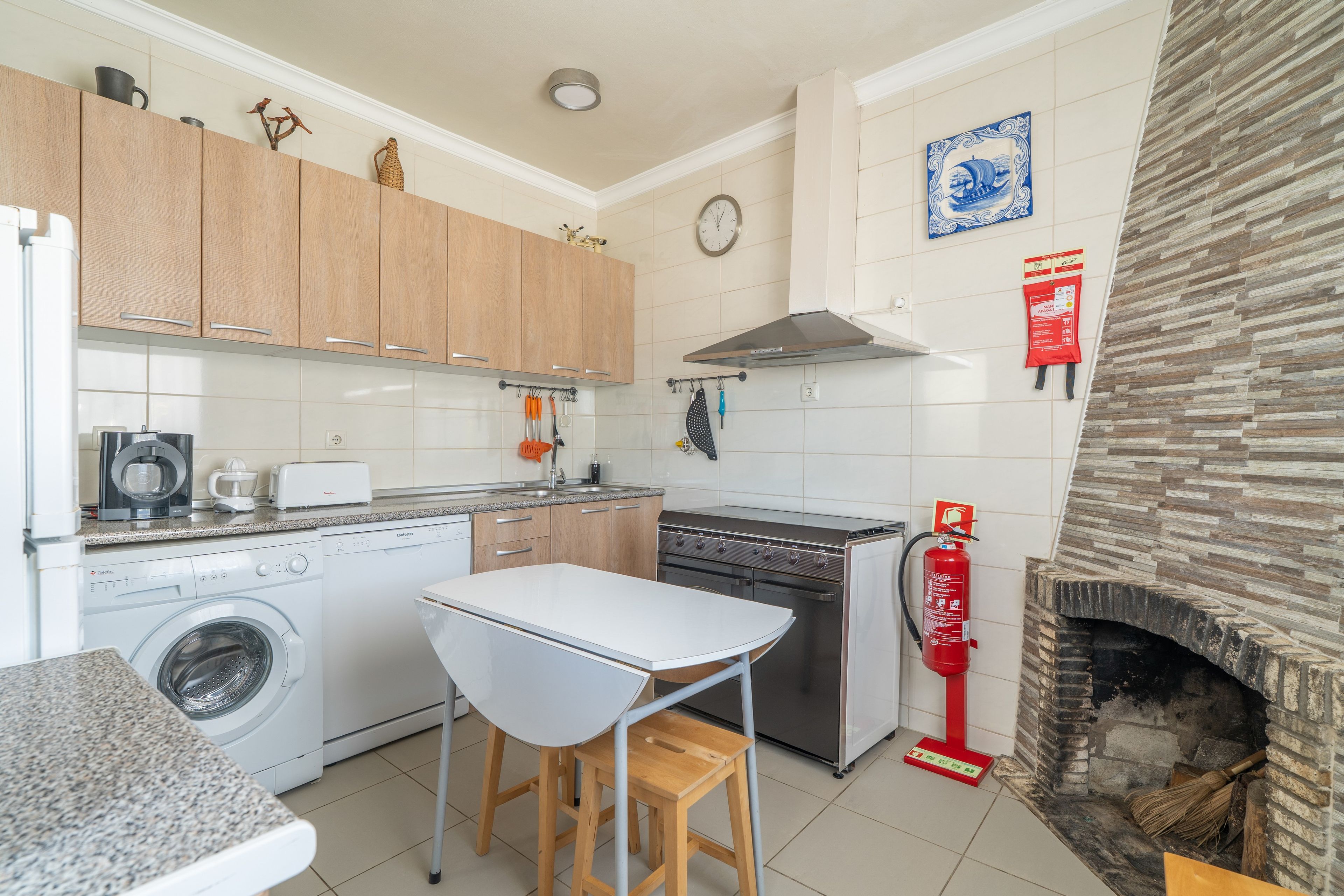 A compact kitchen with a washing machine, a stove, and a fireplace.