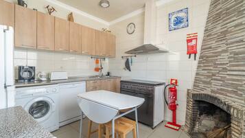 A compact kitchen with a washing machine, a stove, and a fireplace.