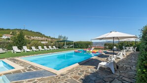 A swimming pool with lounge chairs and umbrellas, surrounded by stone flooring and greenery.